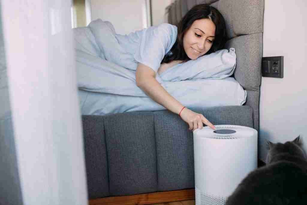 Woman is turning on air purifier in bedroom